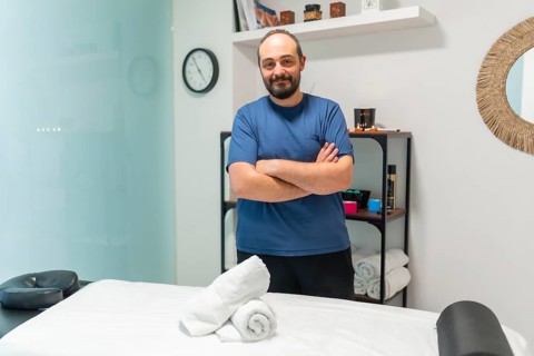 Massage therapist with crossed arms standing in a spa or treatment room, looking at the camera with