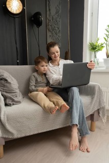 A mother and her son share a bonding moment on a cozy sofa, engaged with a laptop. The scene