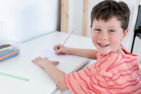 A young boy with a missing front tooth happily engages in drawing activities at a white table at