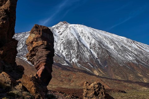 Roques de Garcia, massive rock columns in front of a snow-covered mountain with deep blue sky,