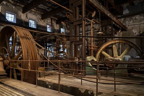 Historic steam engine with large flywheels and rope drive in abandoned meat factory, rusty machine