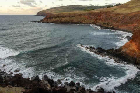 Rocky cliffs with lava rock and surf, reddish volcanic rocks in the evening light, north-east