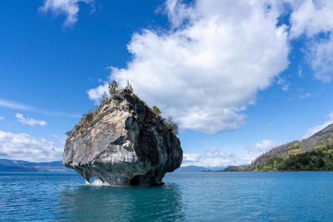 Marble rock of the Capillas de Mármol, overgrown with shrubs, juts out of the turquoise water of