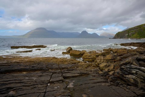 Rocky coastline with waves and views of distant mountains and cloudy sky, Elgol Beach, Elgol, Isle