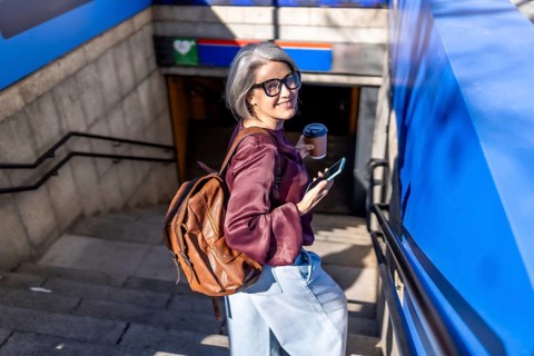 Stylish mature woman with grey hair ascending subway stairs, holding a disposable coffee cup and