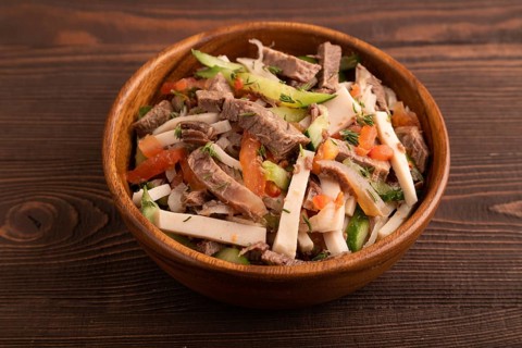 Meat salad with beef and vegetables in wooden bowl on brown wooden background and linen textile.