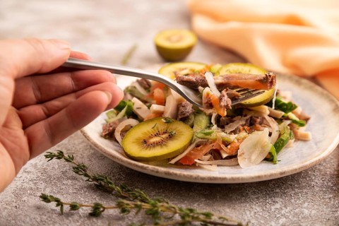 Meat salad with beef kiwi and vegetables with hand on brown concrete background and orange linen