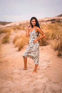 Portrait of a Caucasian brunette stroking her hair in a white flowered dress, in the sand on the