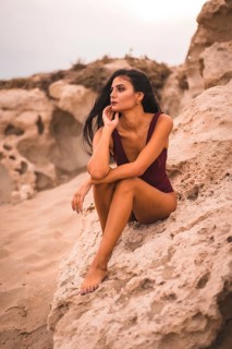 A young brunette Caucasian woman in a maroon swimsuit, sitting on the beach of Cabo de Gata, Nijar.