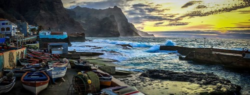 Sunset over a coastal landscape with colorful fishing boats and mountains, romantic harbor scene in