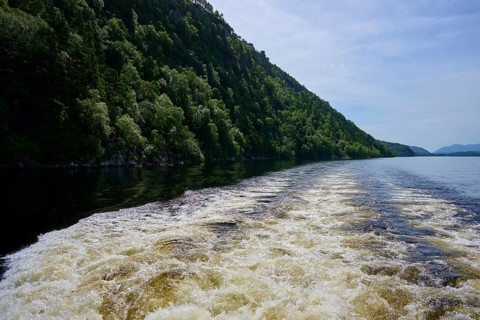 Water flow due to powerboat waves in a river lined with green hills, Fort Augustus, Loch Ness,