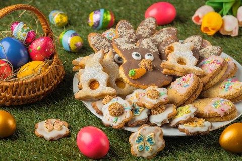 A plate with various Easter cookies and a basket full of colorful Easter eggs, decorated with tulip