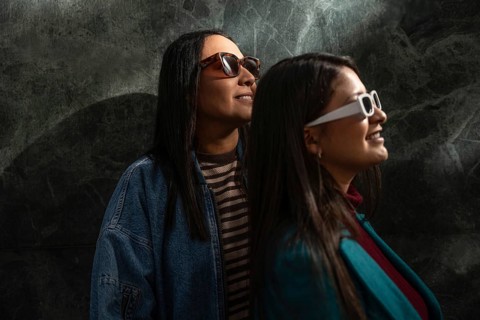 A Latin lesbian couple wearing stylish sunglasses, basking in a joyful moment together. Their