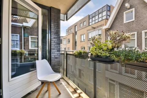 A charming urban balcony features a modern white chair and lush potted plants against a backdrop of