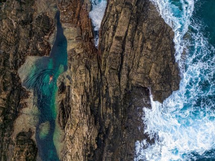 Top view of natural rock pools in Tindaya, Fuerteventura, featuring a woman leisurely swimming in