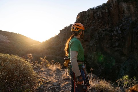 A rock climber, equipped with climbing gear and helmet, stands confidently on a rocky path at