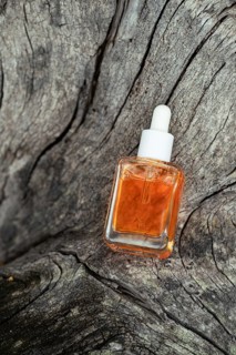 A clear glass bottle of vitamin C serum for face care rests on the textured surface of an old tree