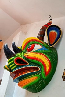 Side view of a colorful Tibetan demon mask with bright psychedelic colors on a wall corner, masks