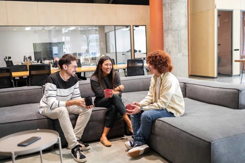 A group of diverse coworkers sits on a comfortable office sofa, engaging in a cheerful conversation