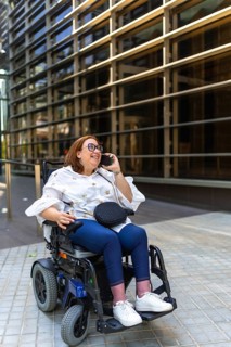 Smiling businesswoman in wheelchair making a phone call in front of a modern office building,