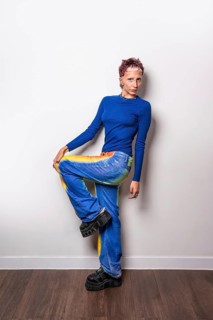 A fashionable young woman poses confidently in trendy, brightly colored trousers and a blue top,