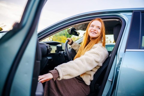 A beautiful pregnant woman with vibrant red hair steps out of a car, smiling brightly. She wears a