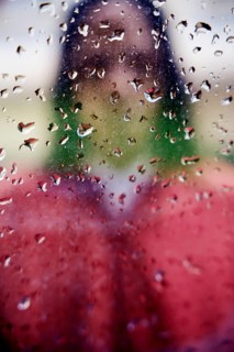 A blurred silhouette of a person visible behind a rain covered glass window. Droplets create an