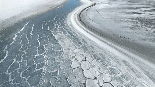 An aerial view of saline mud creates intricate textures and patterns on a vast surface,