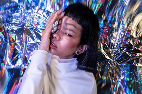 A futuristic Latin woman poses in a metaverse-inspired environment, surrounded by vibrant,