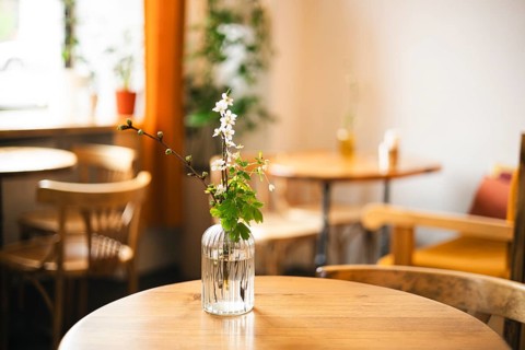 A cozy cafe wooden table with a glass vase holding delicate white flowers. The warm, inviting