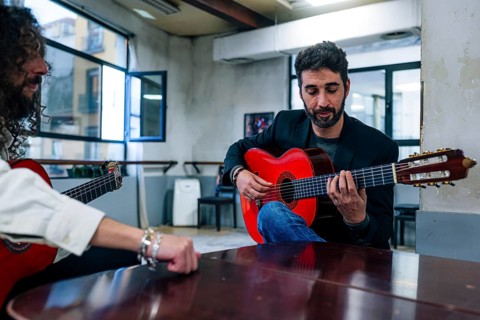 Male friends playing guitars at table in music studio