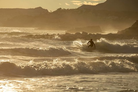 A lone surfer rides the waves against the stunning backdrop of the Costa Blanca, with the golden