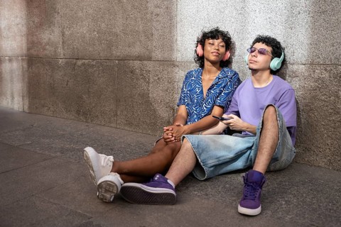 A joyful multiethnic LGBTQ+ couple listens to music with headphones while sitting against a