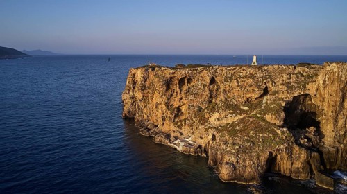 Drone shot, steep cliff by the sea at sunset with calm water and clear sky, morning light, Tsichli