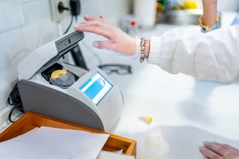 Pharmacist in white coat and gloves operating digital lab equipment to process and analyze a