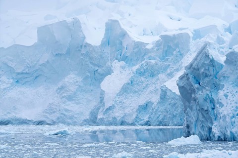 Glacier eruption edge with shimmering blue ice formations, in front of iceberg and floating ice