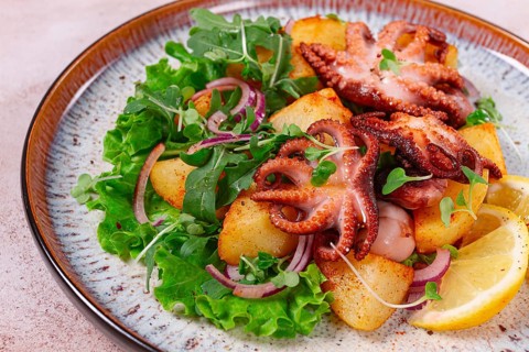 Grilled octopus with baked potatoes and fresh herbs, on a decorative plate, homemade