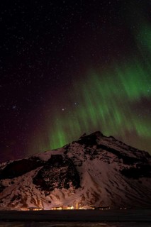 Experience the awe of the Northern Lights casting a green glow over a snow-covered mountain in