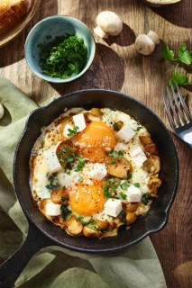 Fried eggs with spinach, mushrooms, grated cheese and feta cheese in small cast iron skillet. Top