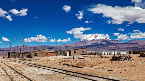 Houses next to train tracks with an impressive volcanic background under clear skies, the town of