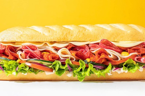 Close-up of a stacked deli sandwich, styled on a vibrant monochrome backdrop, with frontal lighting