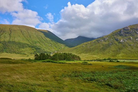Green valleys and mountains under a partly cloudy blue sky surrounded by meadows, Loch Etive,