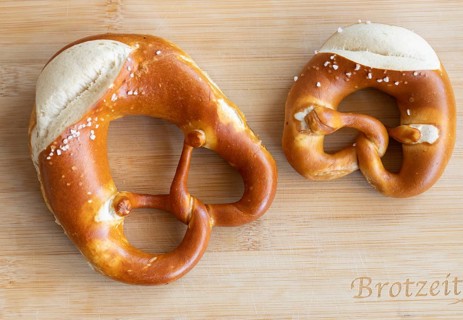 Two pretzels, one craft. Tradition served on a wooden board. A small and a normal pretzel from a