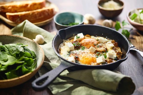Fried eggs with spinach, mushrooms, grated cheese and feta cheese in small cast iron skillet