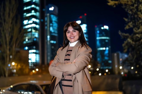 Young woman standing confidently with arms crossed, smiling at the camera outdoors at night, with