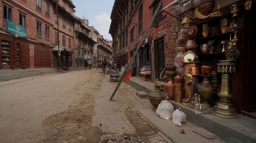 A busy old town street with shops, with a supported façade selling copperware and people walking,