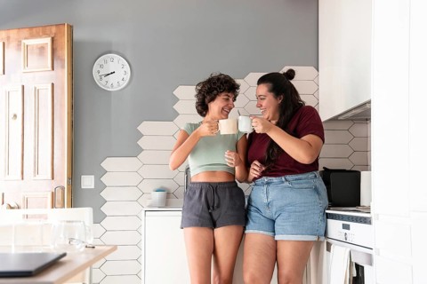 A cheerful lesbian couple shares a coffee break in their stylish kitchen. They enjoy a moment of