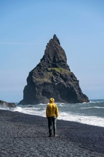 Tourist on black beach, rock Reynisdrangar in water, at Reynisfjara beach, Vik, South Iceland,