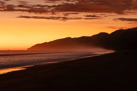 After sunset, the deep red sky glows above palms and ocean spray with views of Corcovado National