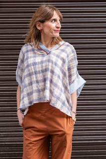 Stylish woman stands confidently in a plaid blouse and brown pants against a striped background.